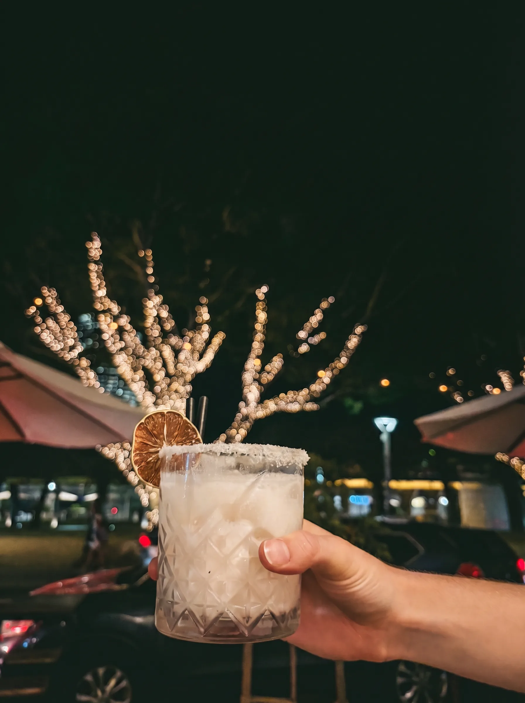 Mango Pina Colada at Poppies Southbank — crystal glass with salt rim and dried lime garnish, South Bank fairy lights in background